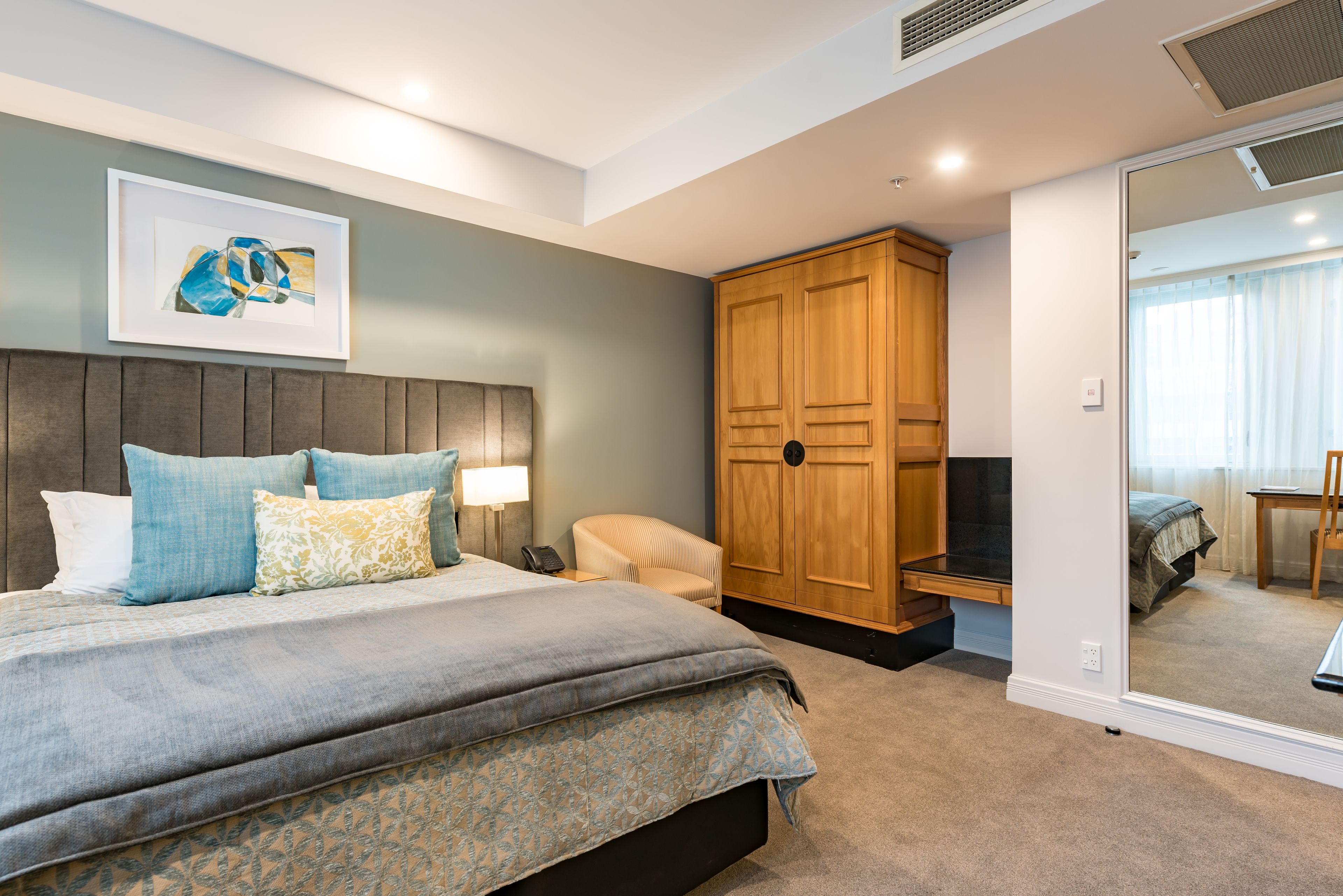 Een slaapkamer met een bed, bedlampen, een houten garderobe en een grote spiegel.