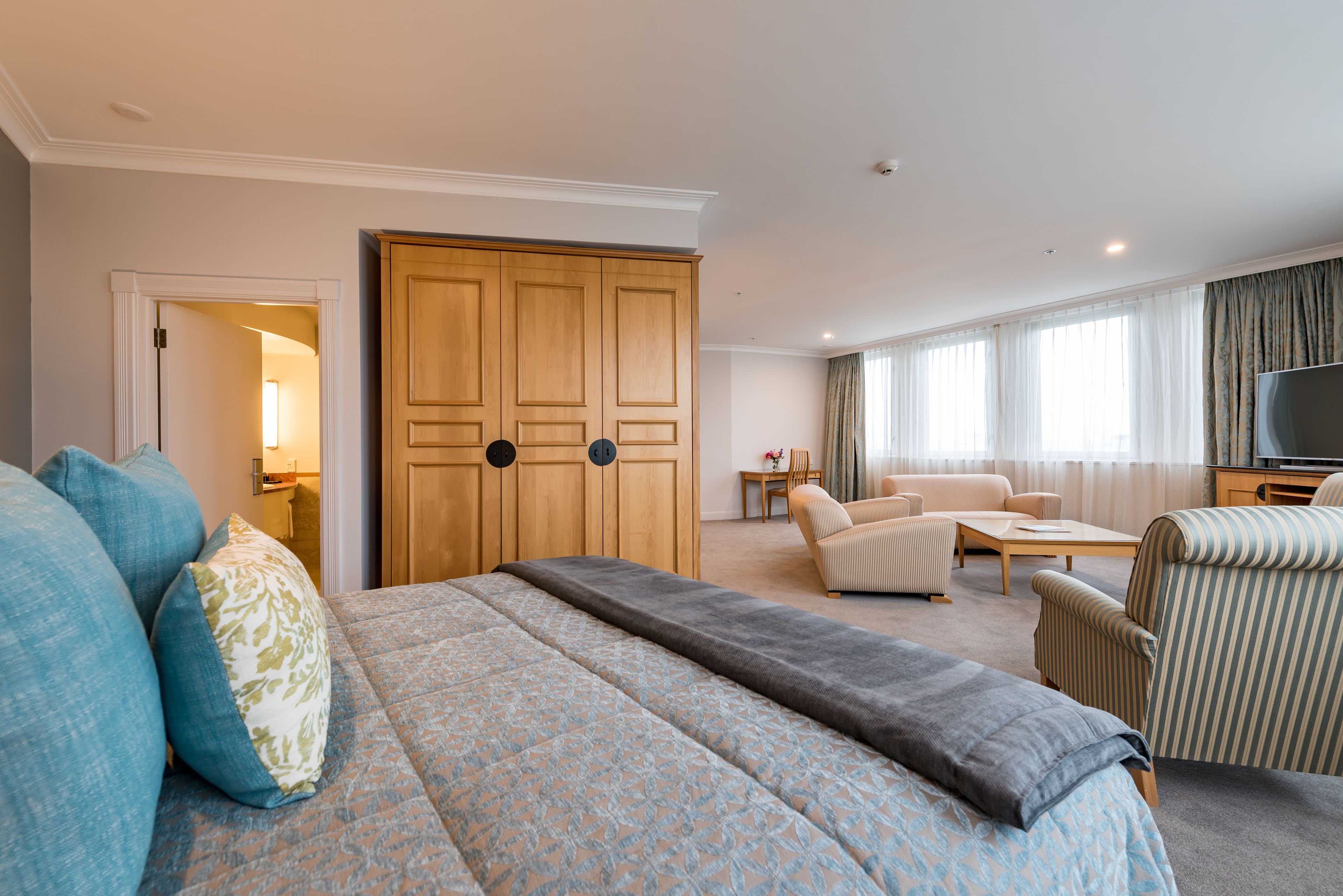 A hotel room with a large bed, a wooden wardrobe, a sofa, a TV, and a small table.