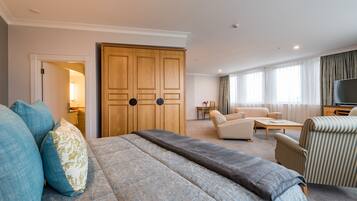 A hotel room with a large bed, a wooden wardrobe, a sofa, a TV, and a small table.