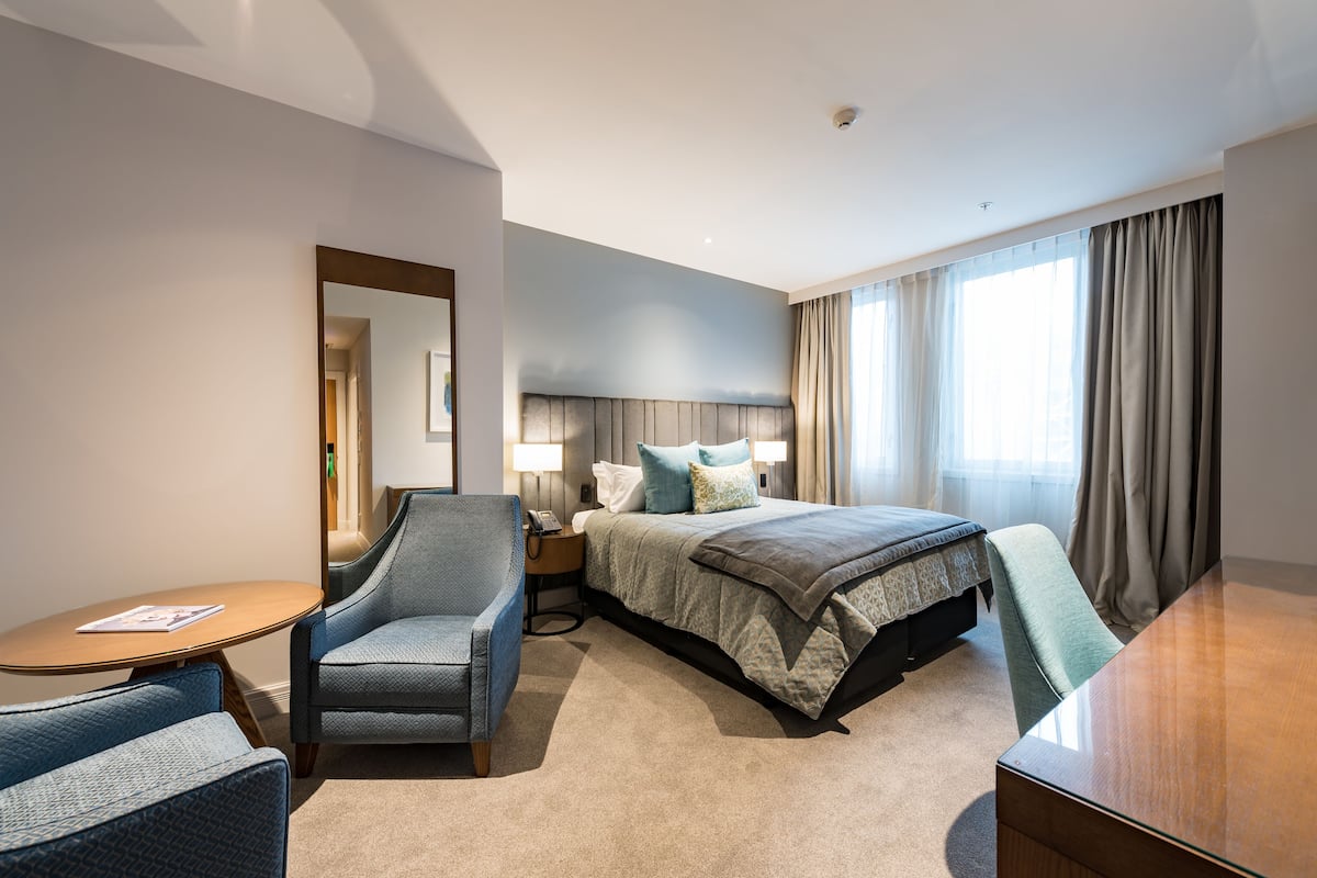 Een hotelkamer met een bed, een stoel, een bureau, een nachtkastje en een spiegel.