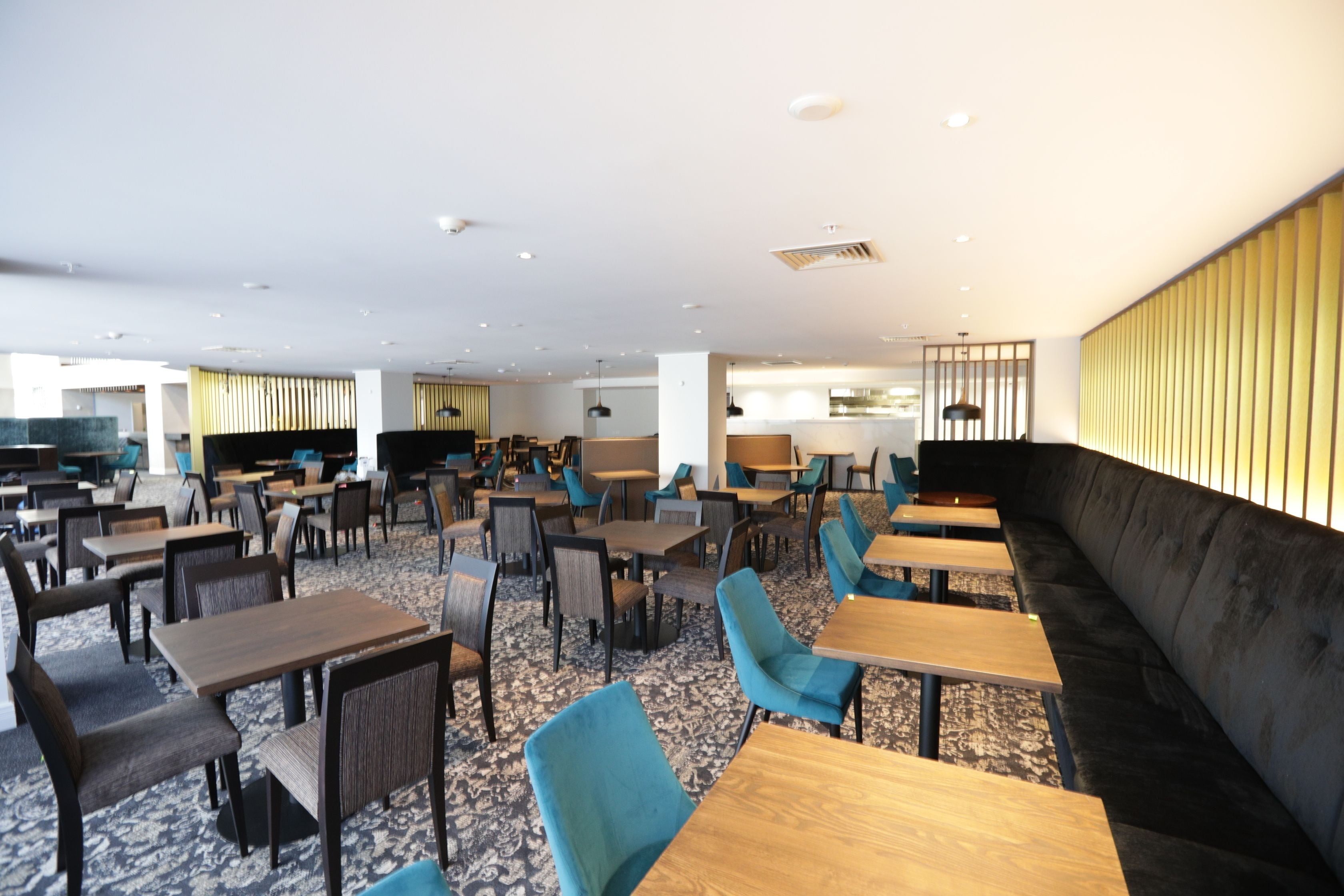 A spacious indoor area with multiple tables and chairs, a large sofa, and a kitchen area in the background.
