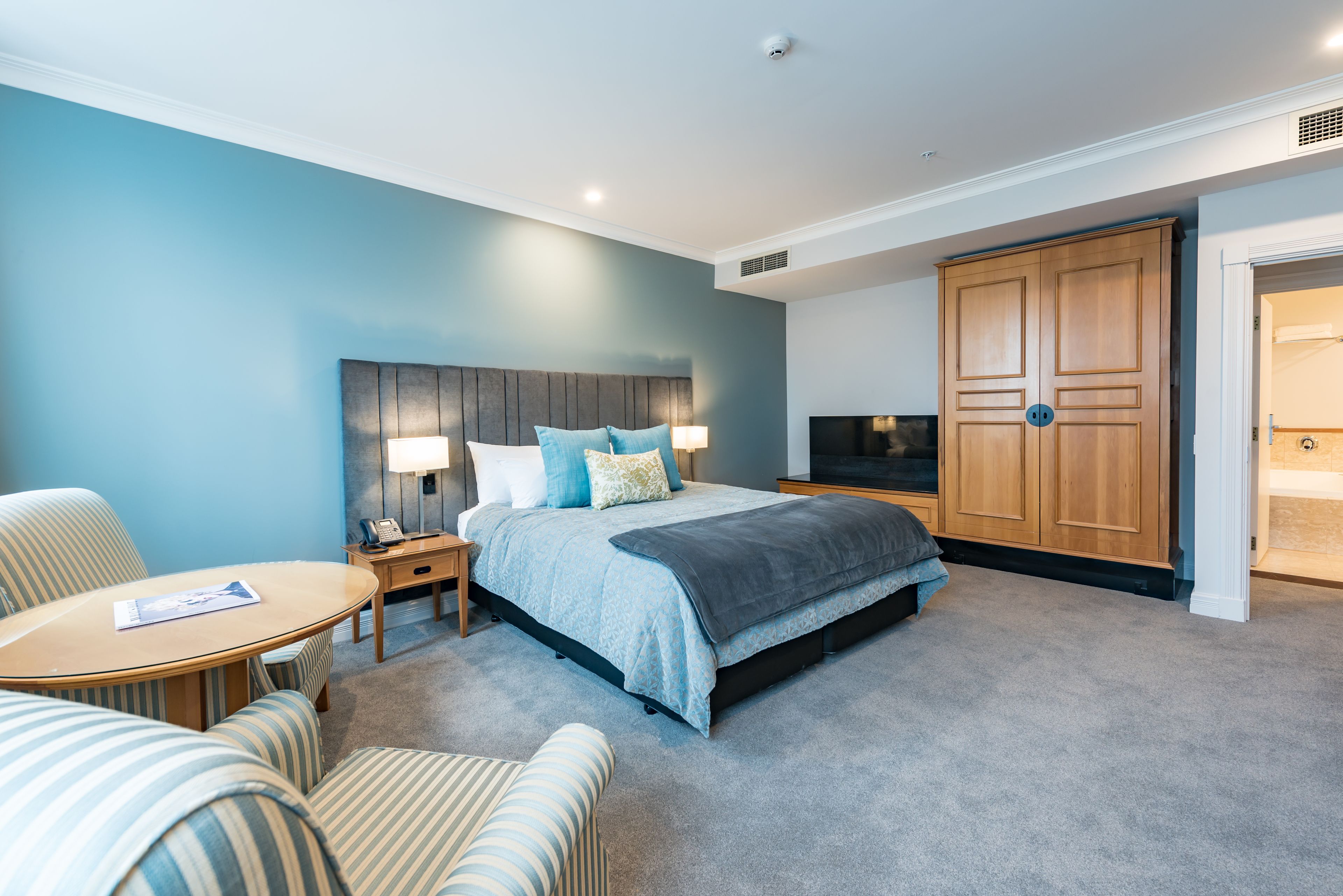 A hotel room with a bed, a desk, a chair, a wardrobe, and a television.