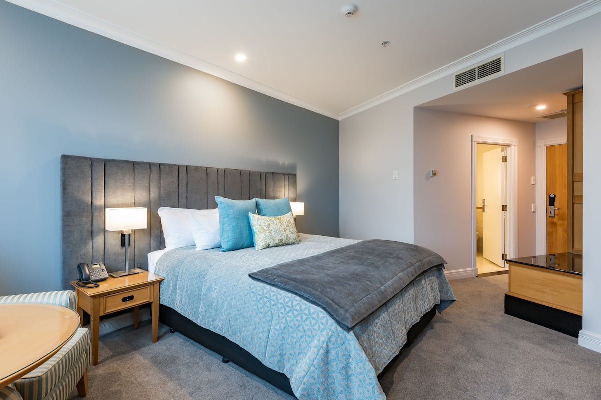 Een slaapkamer met een bed, nachtkastje, lamp en een stoel.