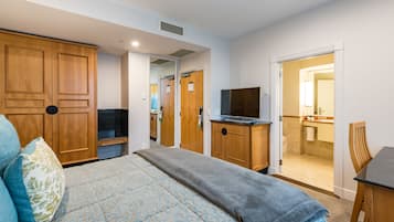Quarto com cama, guarda-roupa de madeira, televisão e banheiro visível através de uma porta aberta.