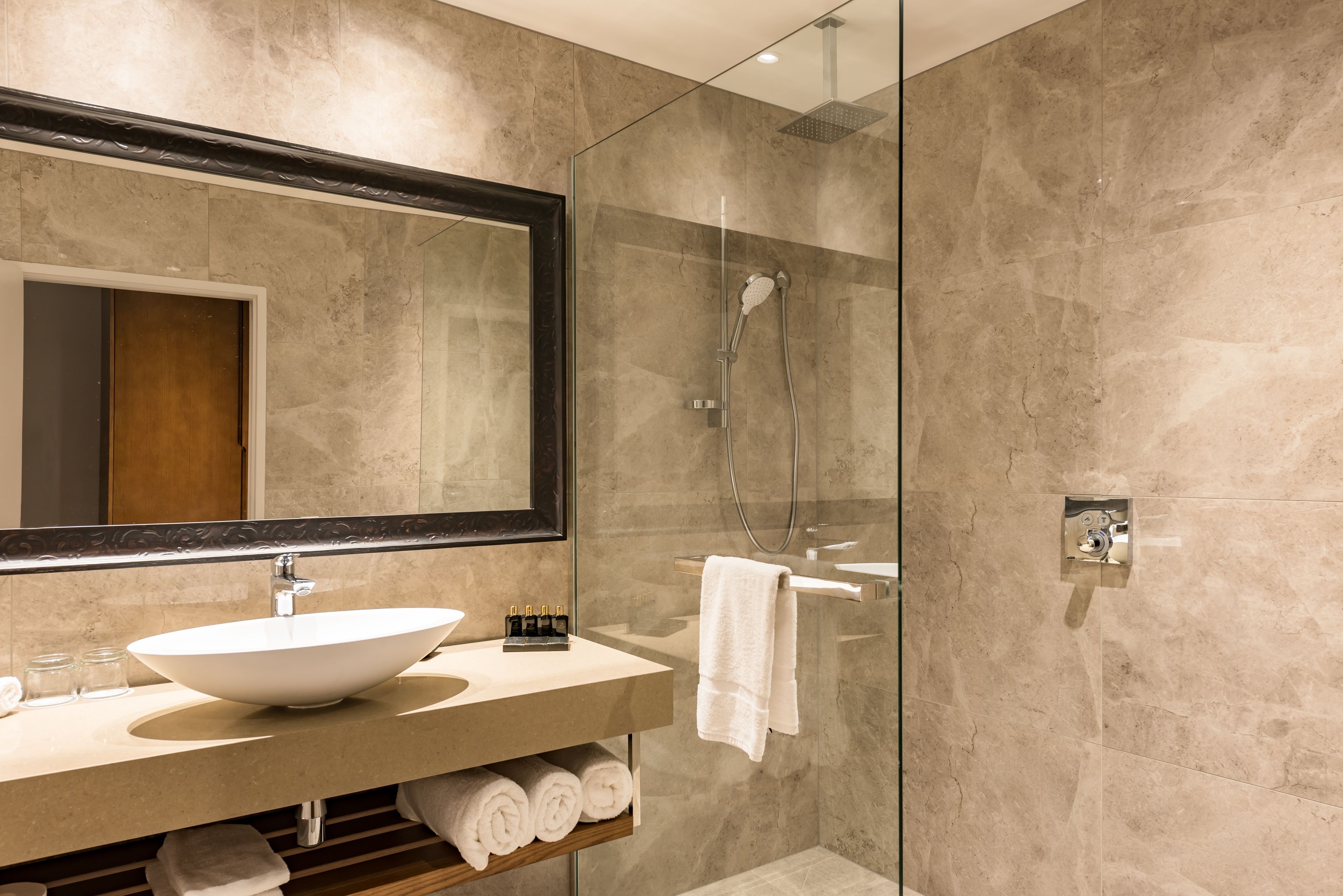 A modern bathroom with a large mirror, a vessel sink, a glass-enclosed shower, and neatly rolled towels.