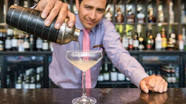 Een barman schenkt een drankje in een martini glas.