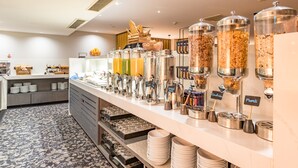 Een buffetgedeelte met diverse voedseldispensers, voorzien van aanduidingen zoals 'Cornflakes' en 'Muesli'.