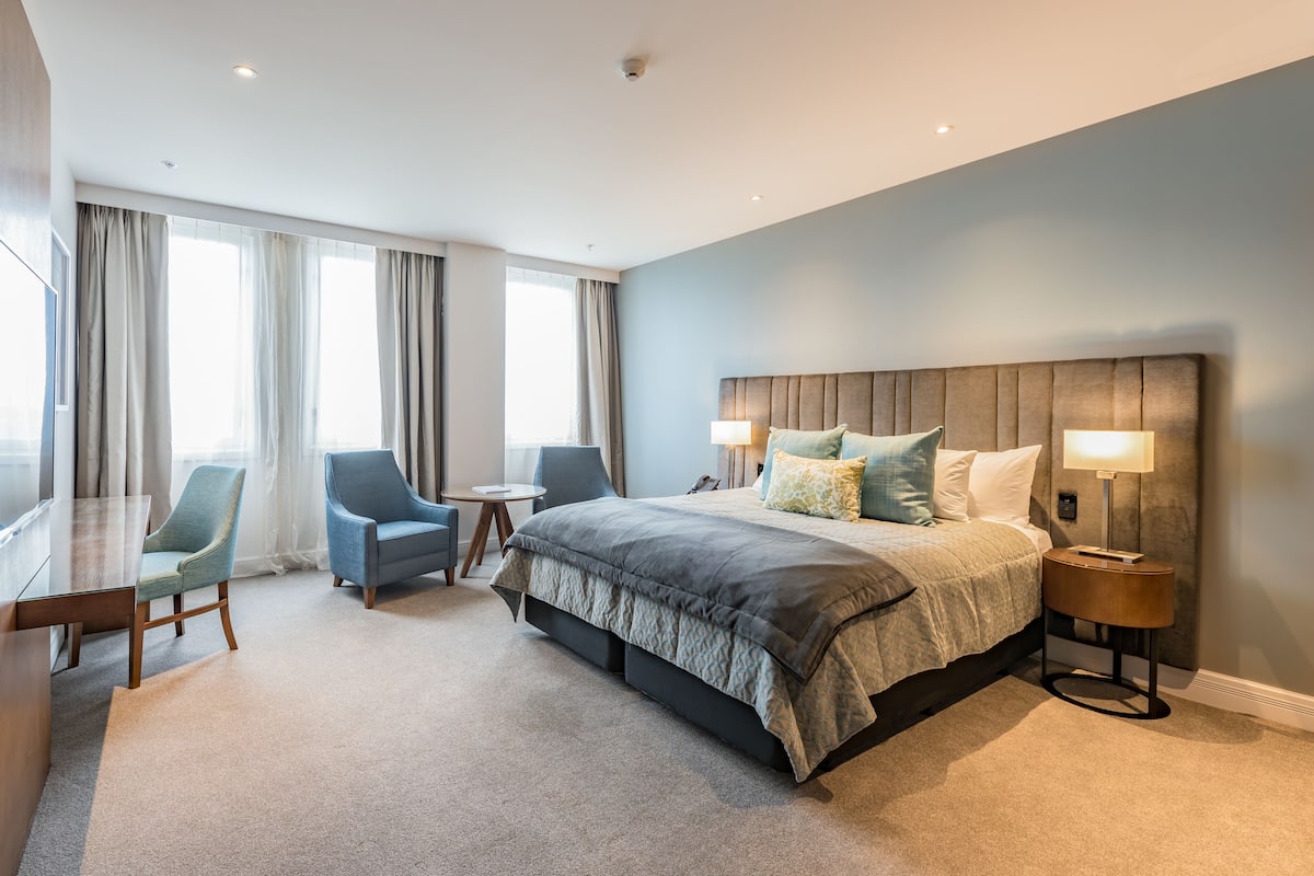 Een moderne hotelkamer met een groot bed, twee stoelen, een bureau en een bijzettafeltje.