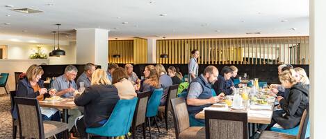 Un comedor con varias mesas y sillas, un camarero atendiendo a los clientes, y una decoración interior moderna.