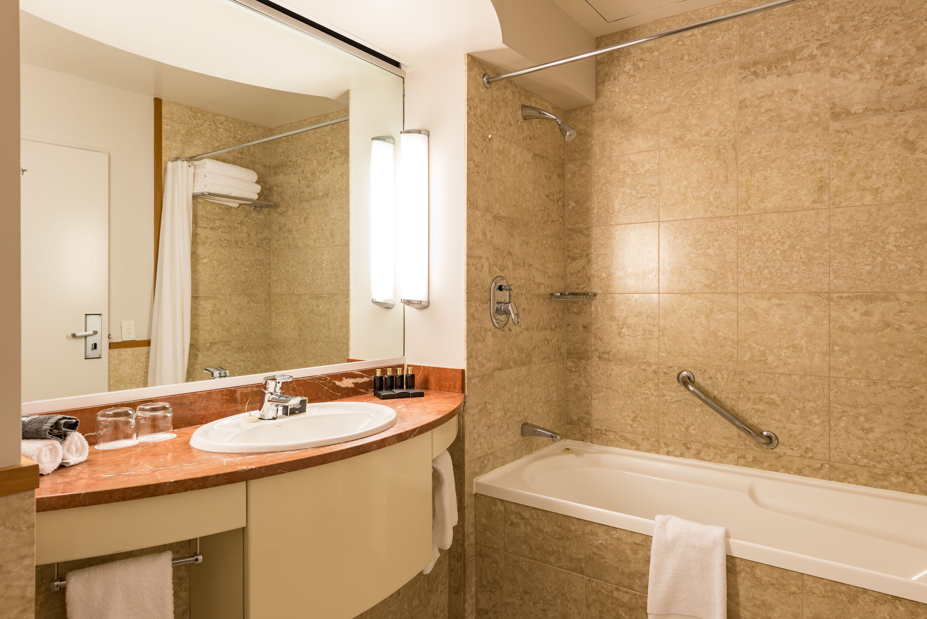 Un baño moderno con encimera de mármol, lavabo, espejo, ducha con barra de apoyo y bañera.