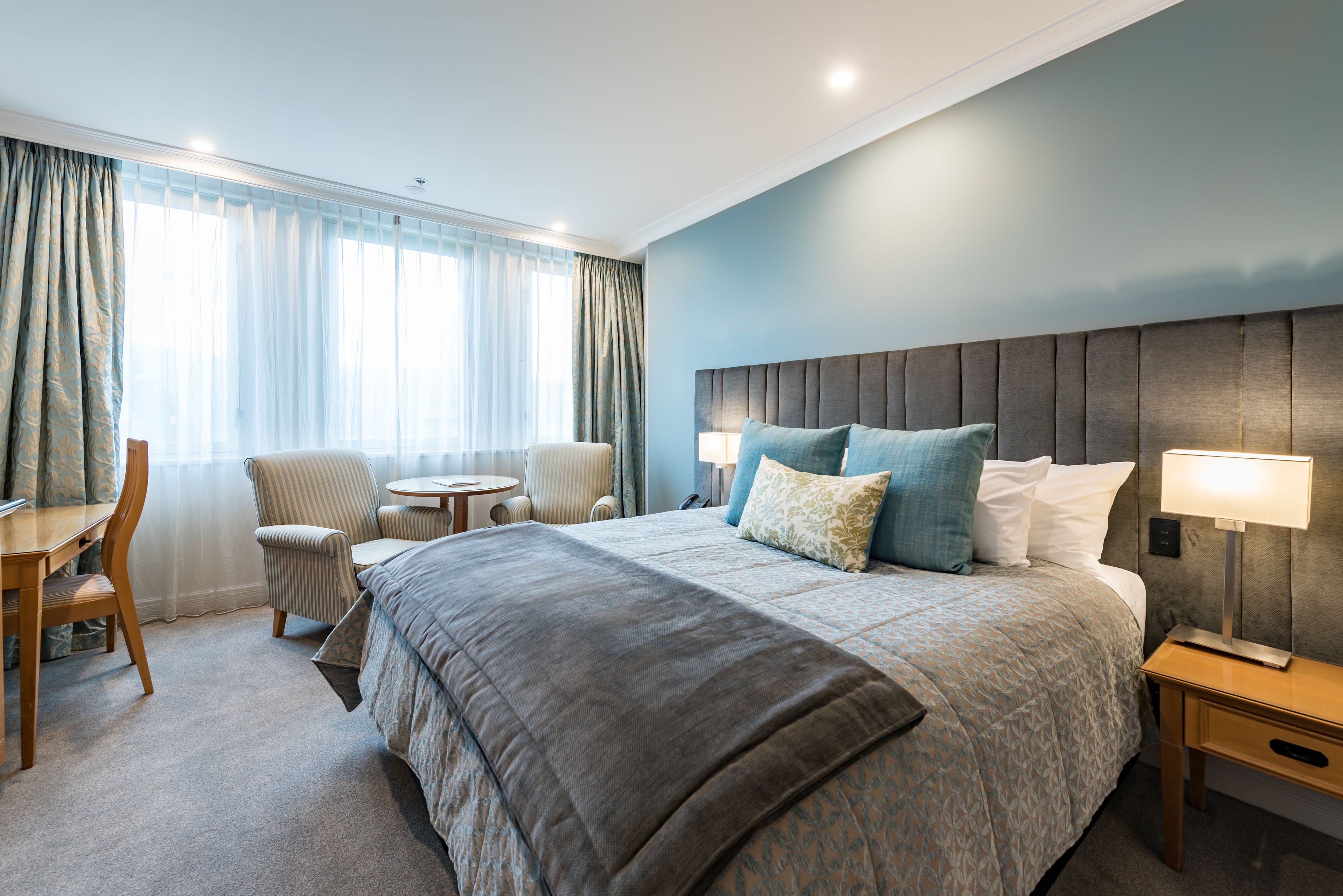 Ein Hotelzimmer mit einem großen Bett, einem Schreibtisch, einem Stuhl und einem kleinen Tisch.