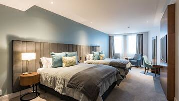 A modern hotel room with two beds, a sitting area, and a large window.