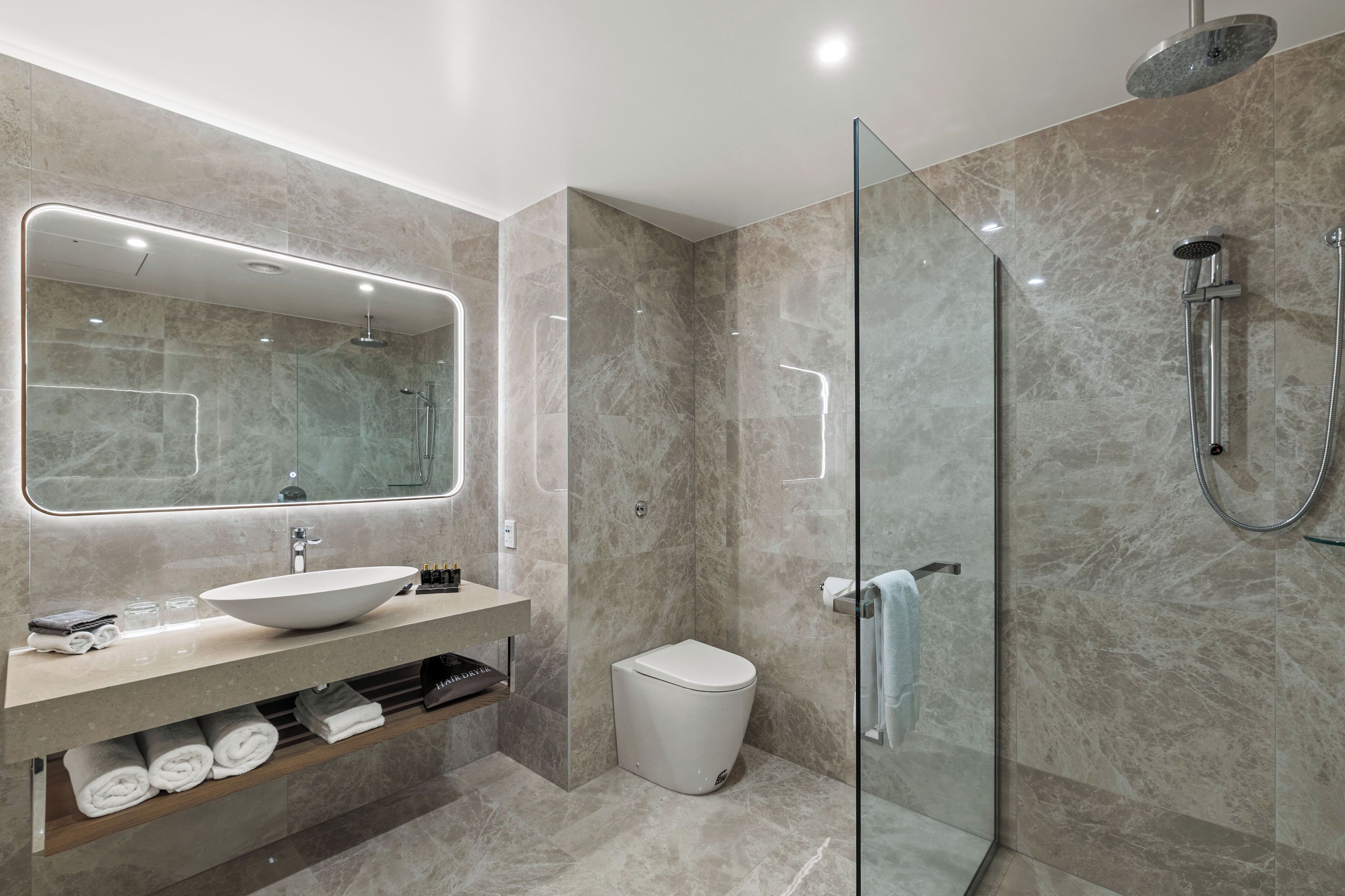 A modern bathroom with a glass-enclosed shower, a large mirror, a vessel sink, and neatly arranged towels.