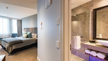 A modern hotel room with a large bed, a separate bathroom with a glass shower, and a view of the city.