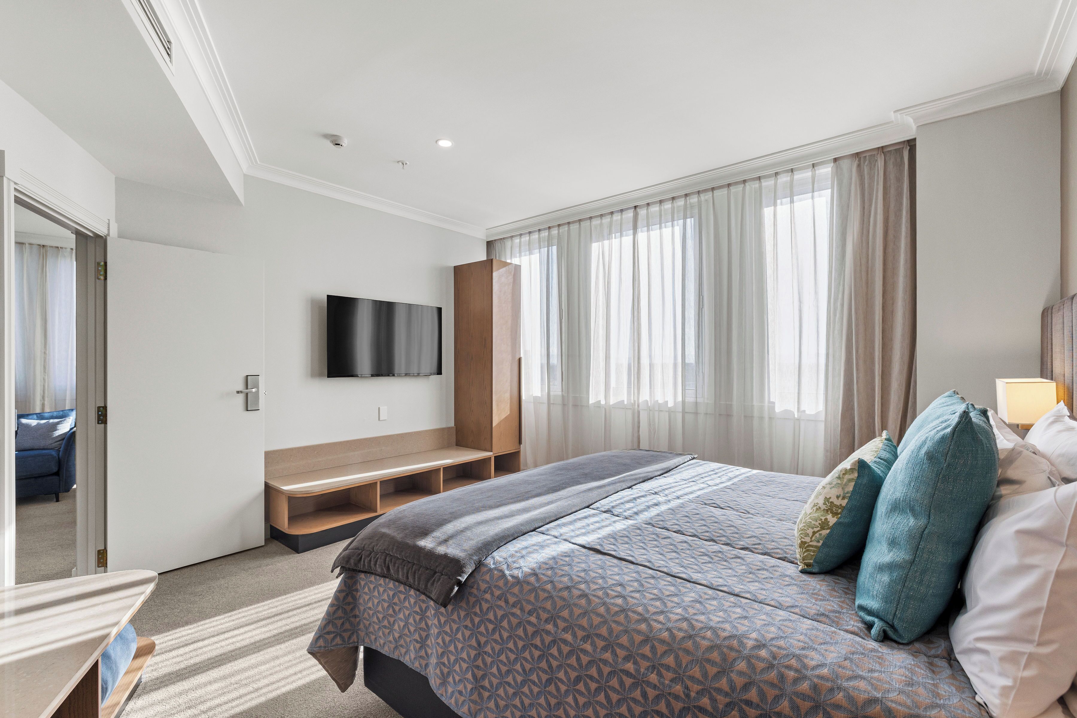A hotel room with a bed, a TV, a desk, and a window with curtains.