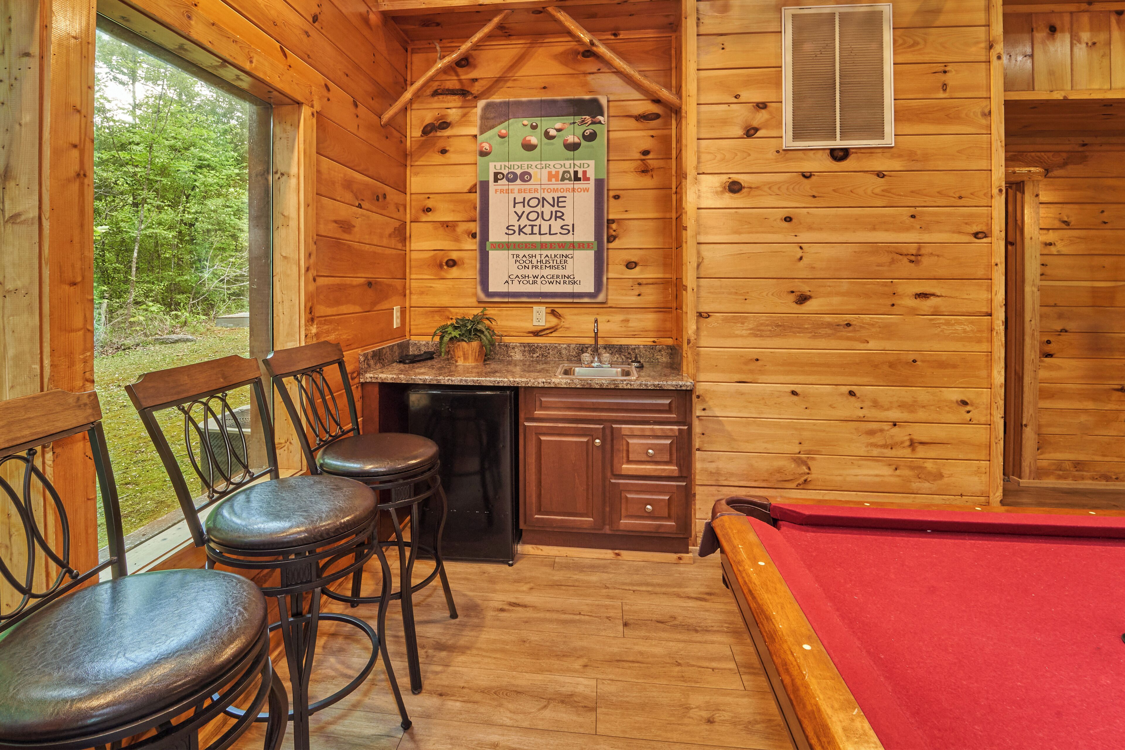 A cozy cabin with a pool table, wooden walls, and a small kitchen area.