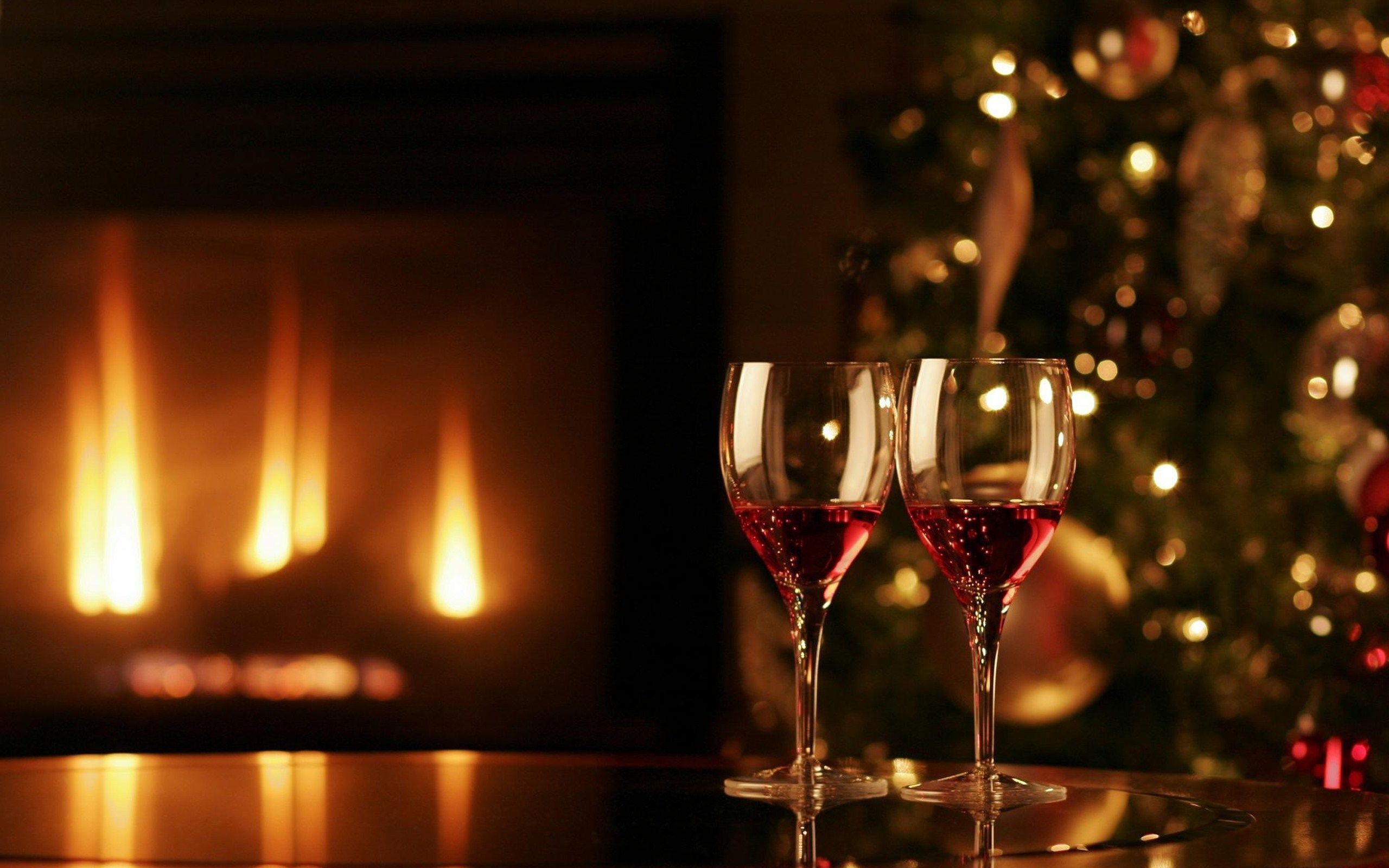 To glas rødvin på en spejlende overflade med en pejs og et pyntet juletræ i baggrunden.