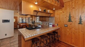 Interior de madera con isla de cocina, taburetes y zona de comedor.