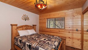 Un dormitorio de cabaña de madera con una cama, una lámpara decorativa en el techo, una ventana con persianas y un reloj de pared.