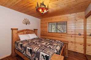 A wooden cabin bedroom with a bed, a decorative ceiling light, a window with blinds, and a wall-mounted clock.