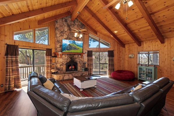 A log cabin interior with a stone fireplace, leather sofas, and a television.