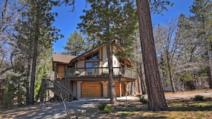 A two-story log cabin with a balcony, garage, and a driveway leading to the entrance.