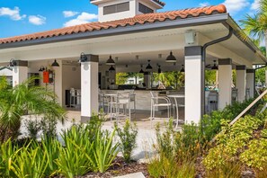 Een overdekt terras buiten met zitplaatsen en een keukenhoek.