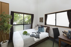 A hotel room with a bed, a desk, a chair, a potted plant, and a window with curtains. - Tranquille Sumiyoshi (Fukuoka)