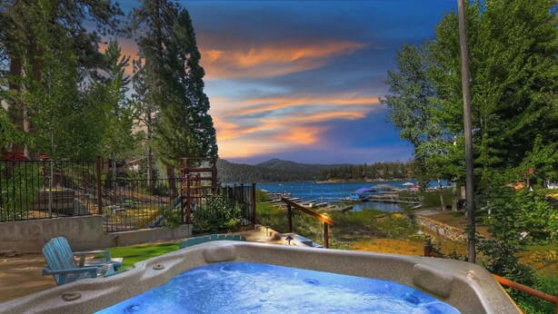 A hot tub with a view of a lake and mountains at sunset.