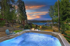 A hot tub with a view of a lake and mountains at sunset.