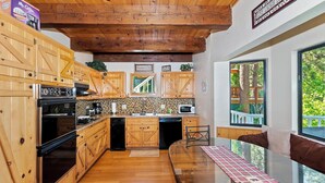 Una cocina con armarios de madera, estufa, lavavajillas y un ventanal con vistas a árboles.