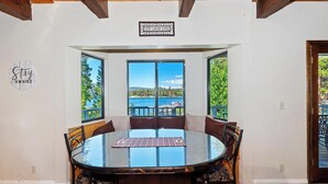 A dining area with a glass table and chairs, large windows with a view of a lake and mountains, and a 'Live Laugh Love' sign on the wall.
