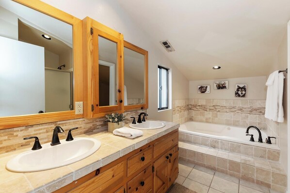 A bathroom with two sinks, a bathtub, wooden cabinets, and a large mirror.