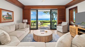 A modern living room with a large sliding glass door leading to a balcony with a view of the ocean.