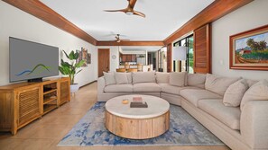 A living room with a sectional sofa, a round coffee table, a TV, and a ceiling fan.