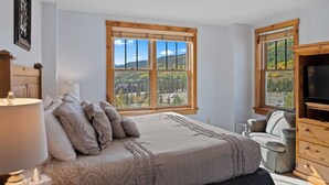A bedroom with a large window, a bed, a chair, and a TV stand. - Views of Decrum Square from Private Balcony, Short Walk to Shops/Gondola/Food (Keystone)