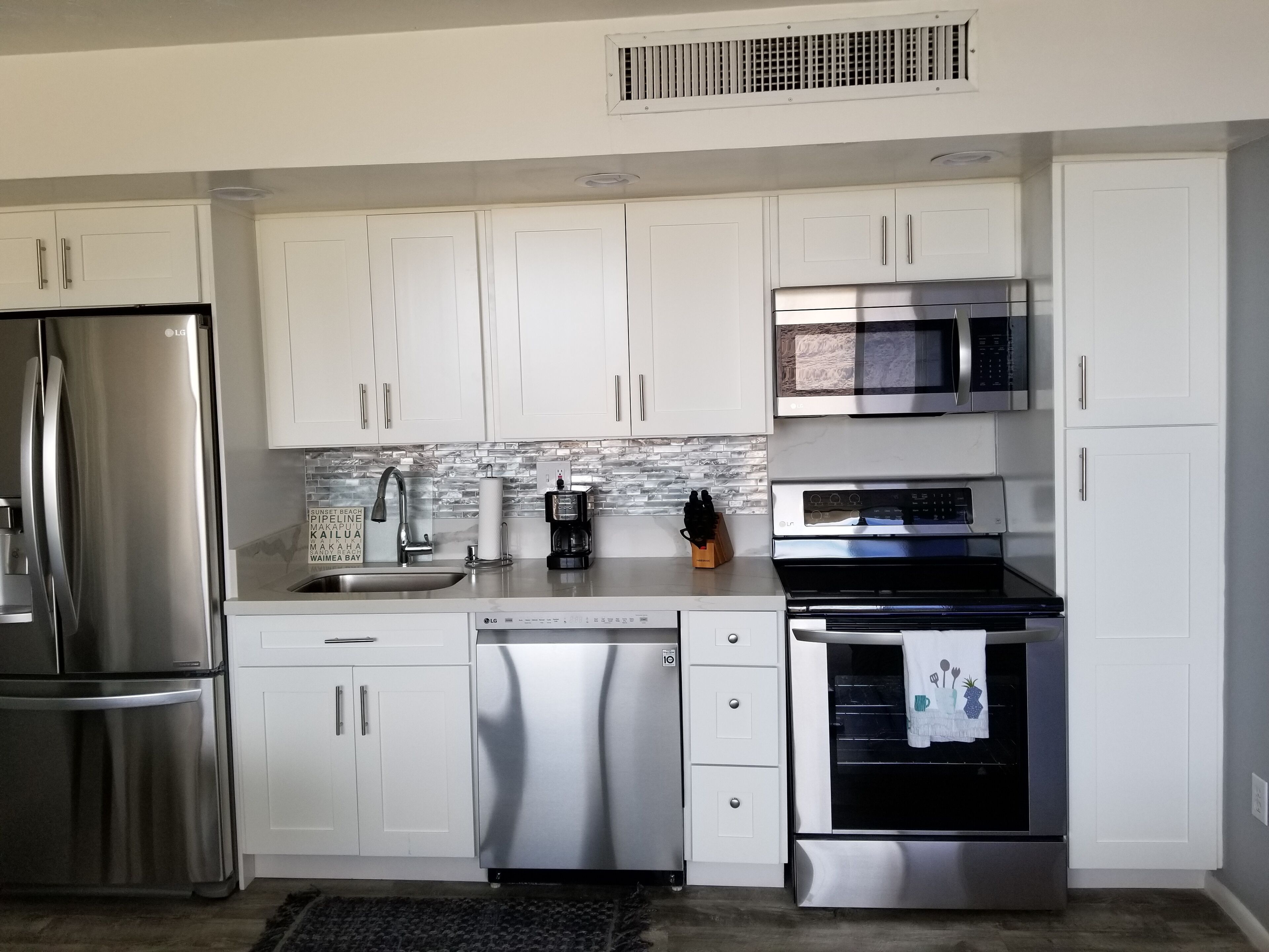 A modern kitchen with stainless steel appliances, white cabinetry, and a tiled backsplash.