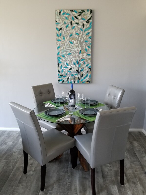 Una mesa de comedor con cuatro sillas, superficie de vidrio y un adorno en la pared superior.