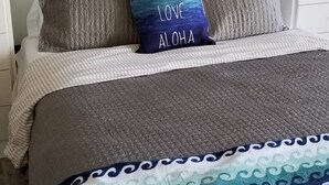 En snyggt bäddad säng med ett vadderat grått täcke och en blå och vit pläd med vågmönster.
