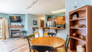 Una sala de estar acogedora con chimenea, una mesa de comedor de madera y sillas. Se observa un área de cocina con armarios de madera y un refrigerador.