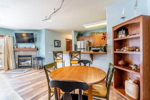 Una sala de estar acogedora con chimenea, una mesa de comedor de madera y sillas. Se observa un área de cocina con armarios de madera y un refrigerador.