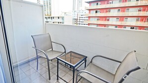 Un balcon avec deux chaises et une petite table, donnant sur un paysage urbain avec de hauts immeubles.