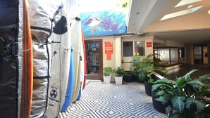 Un hall d’hôtel décoré de planches de surf, avec un panneau indiquant le lieu de dépôt des bagages et des plantes en pot.