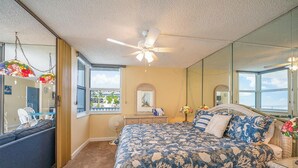 Un dormitorio con una cama grande, ventilador de techo, ventana con vistas, cómoda y espejo.