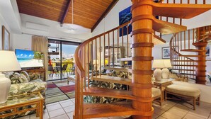 Un vaste salon agrémenté d’un escalier en colimaçon en bois, d’un grand téléviseur à écran plat et offrant une vue sur la plage grâce à une porte vitrée.