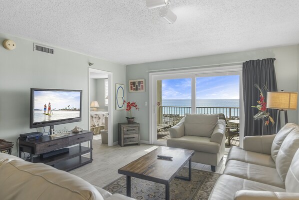 A living room with a TV, sofa, coffee table, and a view of the ocean.
