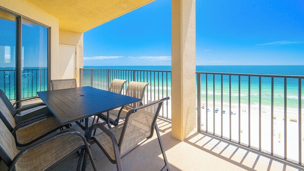 A balcony with a table and chairs, overlooking a beach with clear blue water and a sandy shore. - **WEEKLY SPECIALS!** Phoenix V - 14th Floor - 3 Bedroom (Orange Beach)
