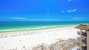 A beach with umbrellas and lounge chairs, a clear sky, and a building with balconies. - **WEEKLY SPECIALS!** Phoenix V - 14th Floor - 3 Bedroom (Orange Beach)