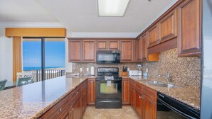 A kitchen with granite countertops, wooden cabinets, a microwave, stove, and dishwasher. - **WEEKLY SPECIALS!** Phoenix V - 14th Floor - 3 Bedroom (Orange Beach)