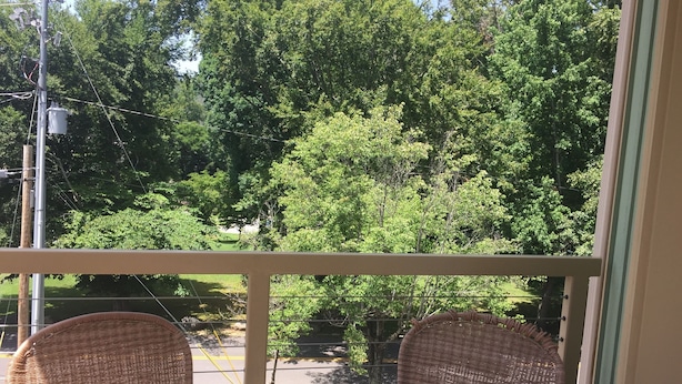 A balcony with wicker chairs and a view of a green park.